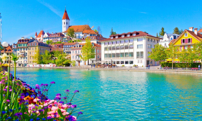 Cidade à beira de um lago, com casas coloridas, uma igreja ao fundo e flores em primeiro plano.Cidade à beira de um lago, com casas coloridas, uma igreja ao fundo e flores em primeiro plano.